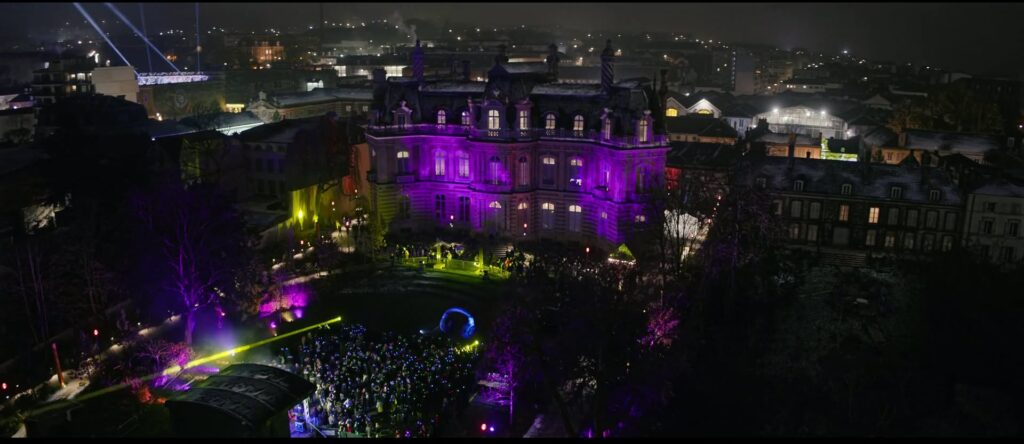 Vue aérienne d'une silent party : invités avec casques lumineux devant un château illuminé